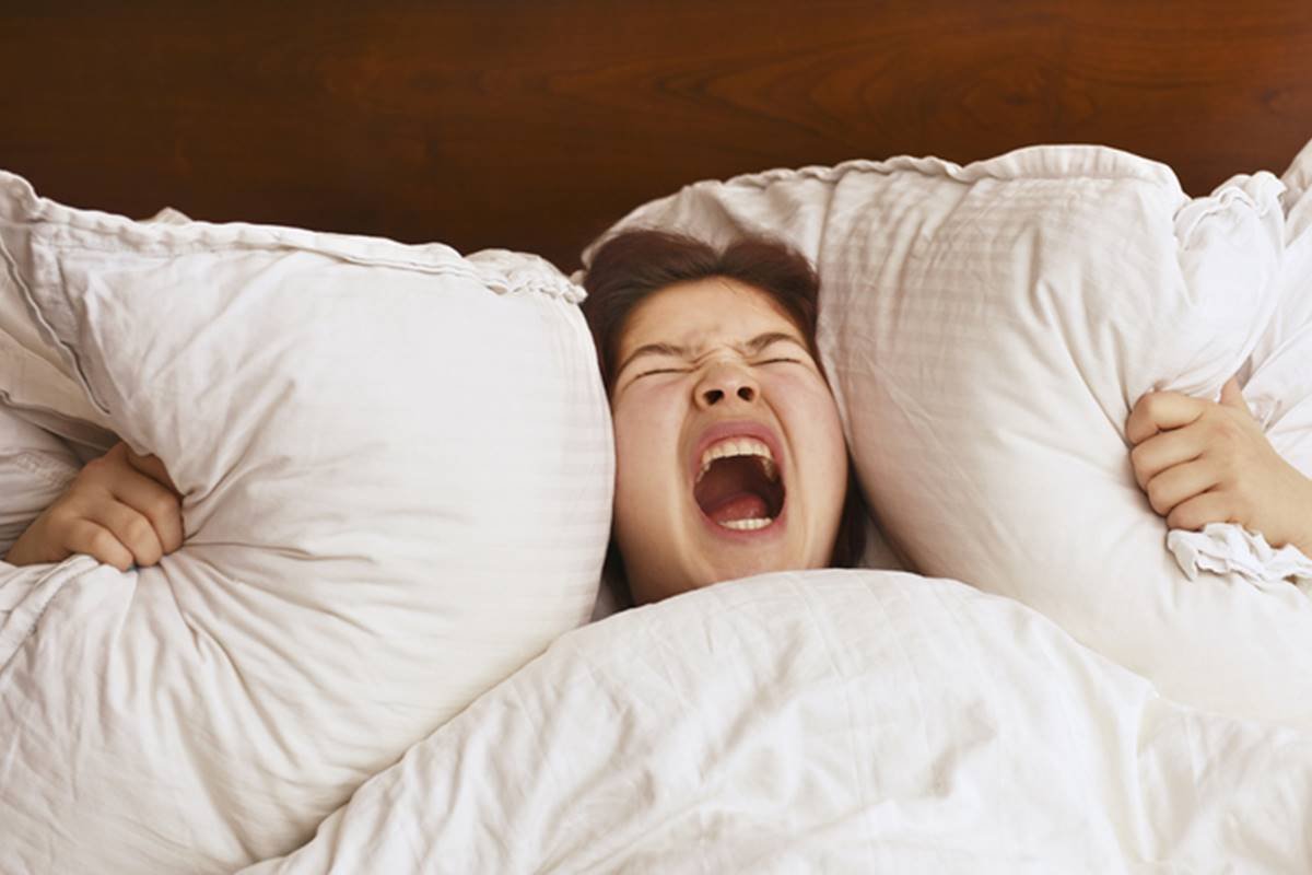 Imagem coloridade de menina deitada de barriga para cima com expressão facil de grito enquanto aperta travesseiro - Metrópoles