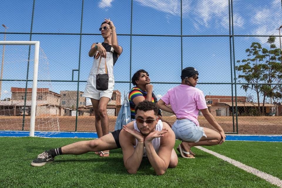 Quatro pessoas em um gramado de futebol fazendo poses. Ao fundo, a Cidade Estrutural - Metrópoles