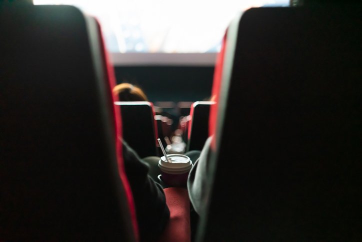 Imagem de sala de cinema, com poltronas vistas de trás e pessoas sentadas assistindo a um filme - Metrópoles