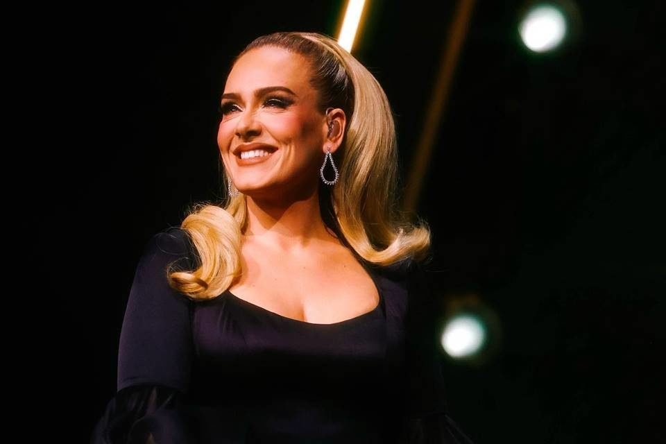 Foto colorida da cantora Adele no palco sorrindo e olhando para frente - Metrópoles