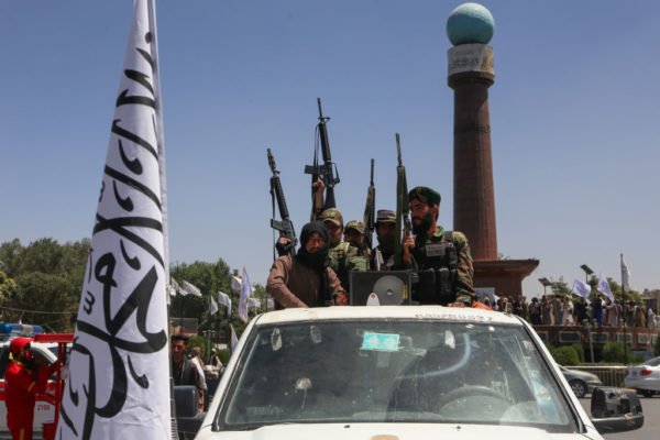Imagem colorida mostra integrantes do Talibã em um carro ao lado de uma bandeira do grupo islâmico - Metrópoles