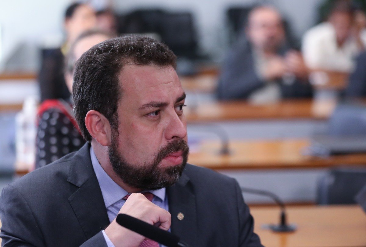 Imagem colorida mostra o deputado Guilherme Boulos em um dos auditórios da Câmara. Homem branco, de cabelo e barba castanhos, ele veste terno cinza - Metrópoles