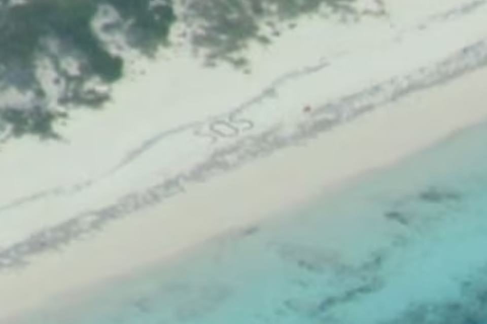 Foto colorida de "SOS" escrito em areia de praia nas Bahamas - Metrópoles