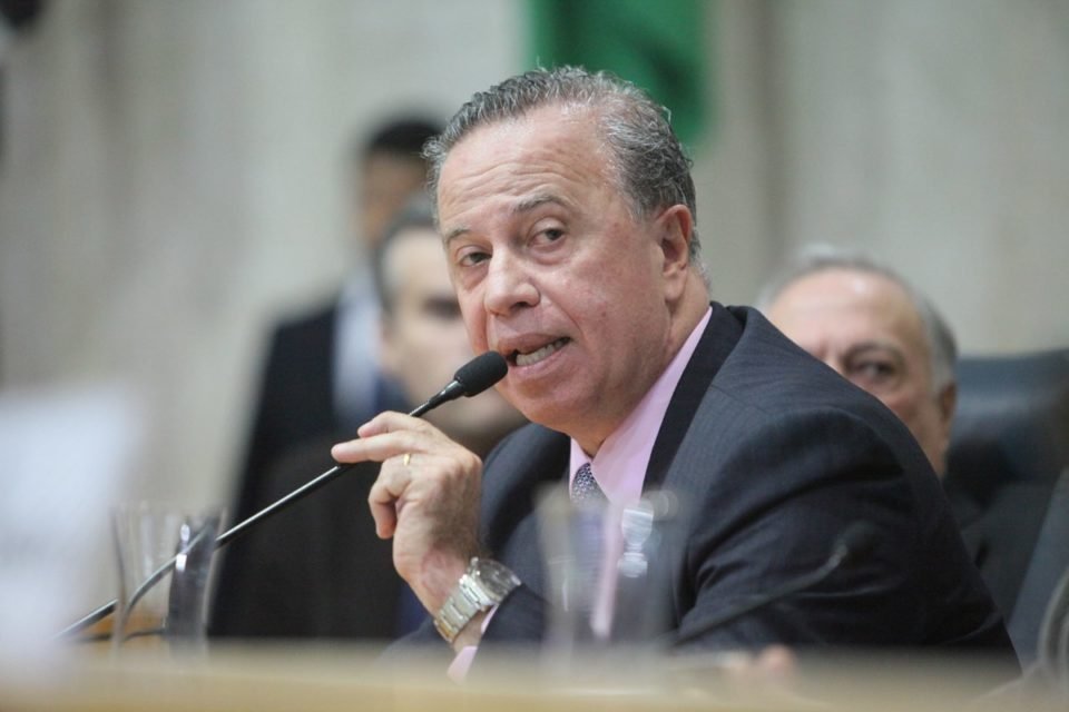 Imagem colorida mostra Camilo Cristófaro, homem branco, grisalho, de terno, falando ao microfone na Câmara Municipal