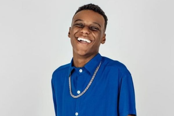 Foto colorida de Samuel Minervino. Ele é um homem negro, está sorrindo, usa camisa azul de botão e uma corrente prata - Metrópoles