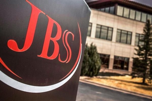 Imagem da fachada de unidade da JBS, com logotipo da empresa, em letras na cor vermelha e fundo branco, e um prédio atrás - Metrópoles