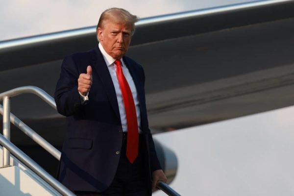 imagem colorida mostra donald trump descendo de avião usando terno preto com gravata vermelha - Metrópoles