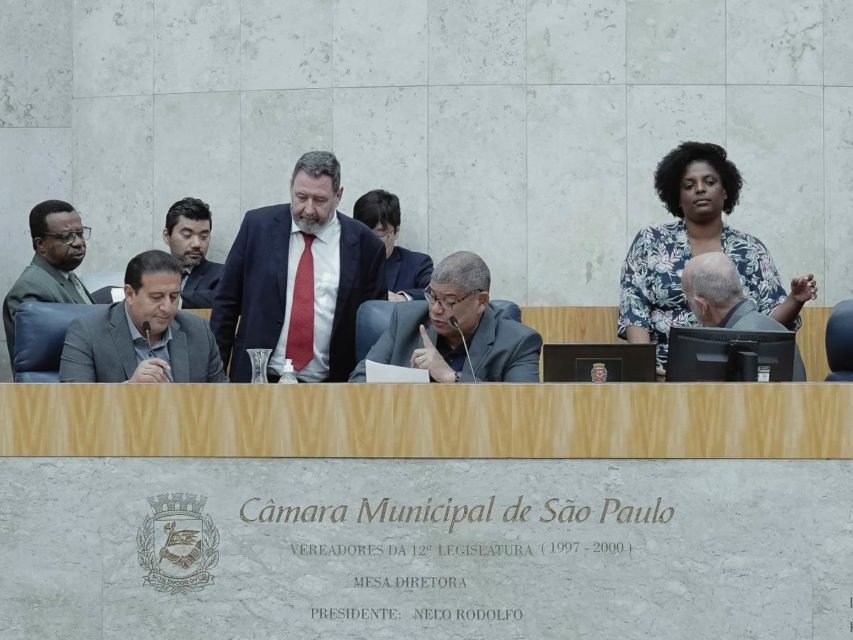 Imagem colorida mostra a mesa diretora do plenário da Câmara Municipal de SP com grupo de vereadores conversando - Metrópoles