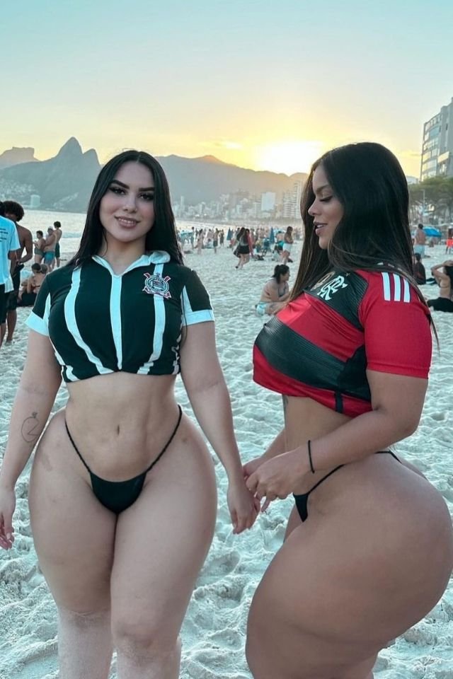 Foto colorida de duas mulheres em praia usando blusa de time - Metrópoles