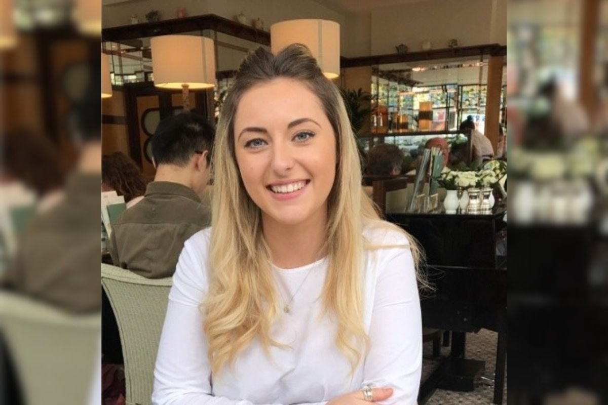 Imagem colorida de mulher de branco sentada em restaurante enquanto sorri para foto