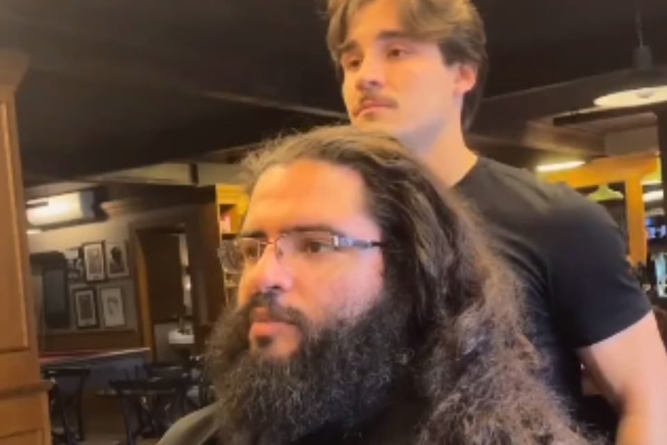 Foto colorida de um homem com cabelo grande na barbearia - Metrópoles