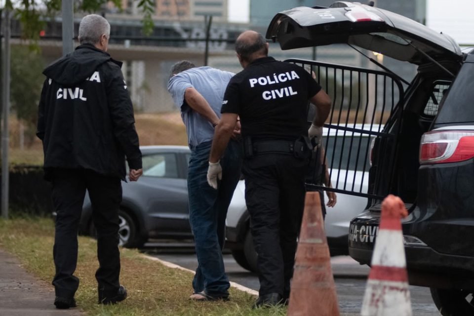 Homem de camisa cinza é retirado de viatura por policiais