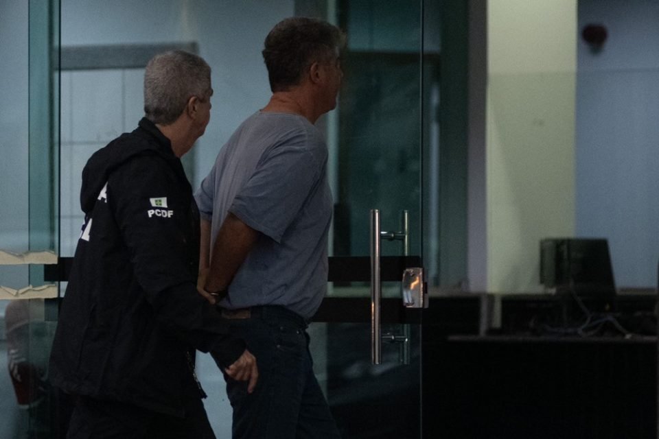 Homem de camisa cinza é levado por policiais