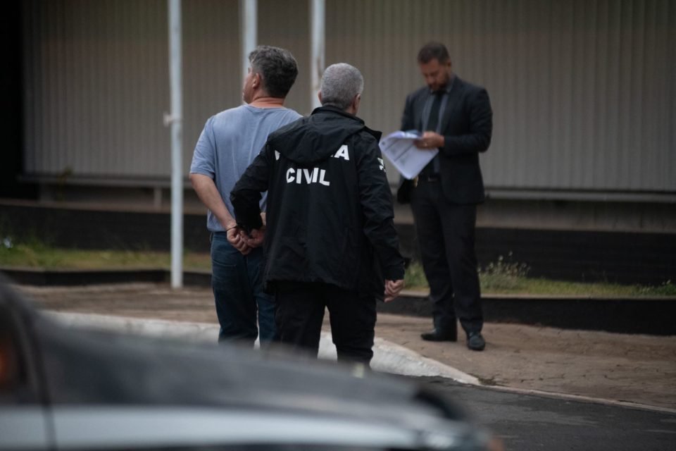 Homem de camisa cinza é levado por policiais