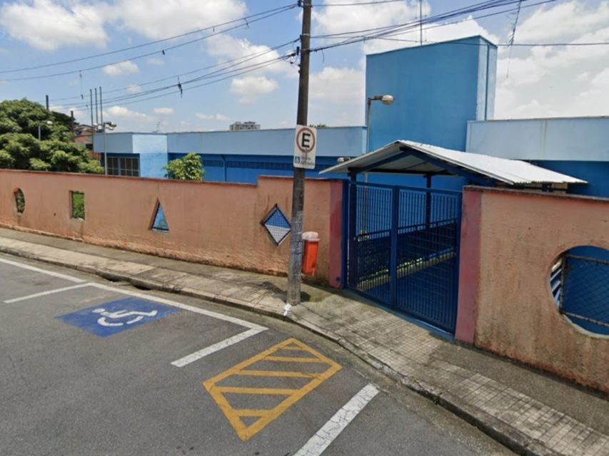 Foto colorida mostra fachada de escola com muro vermelho e portão azul.