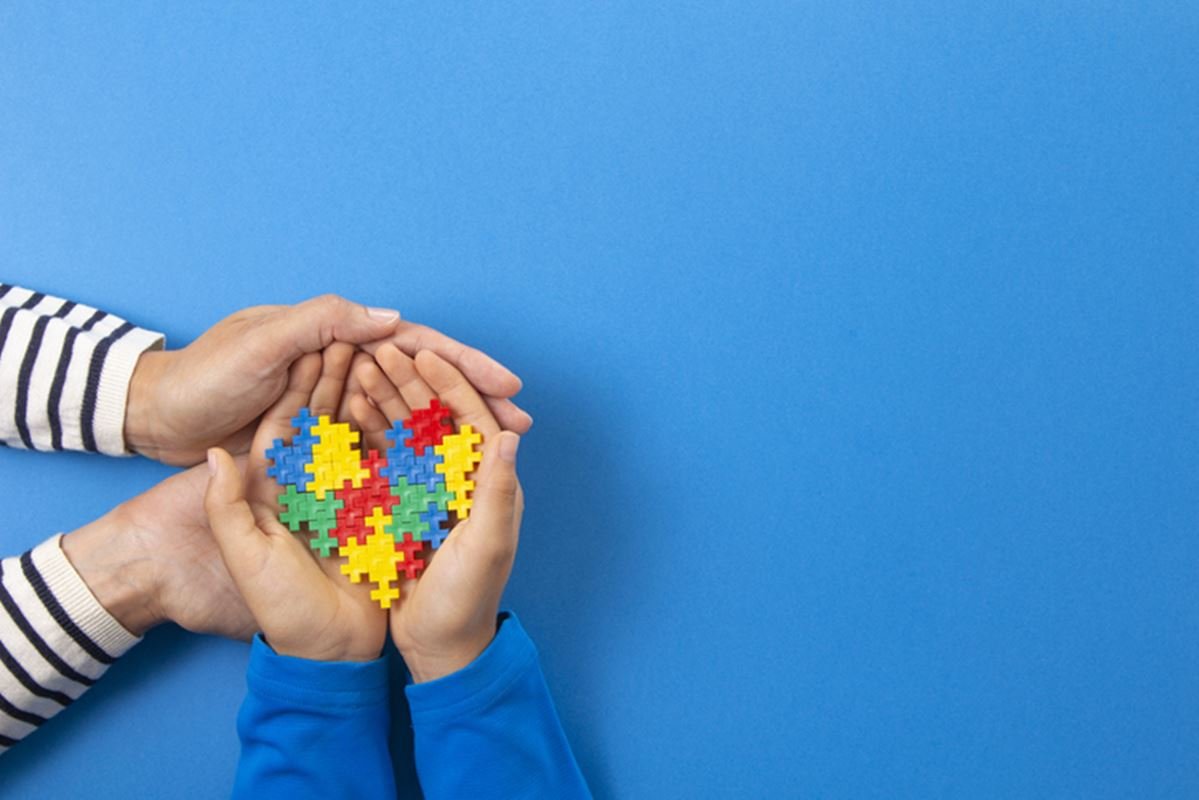 Foto colorida de duas mãos segurando pelas de quebra-cabeça, símbolo do autismo - Metrópoles