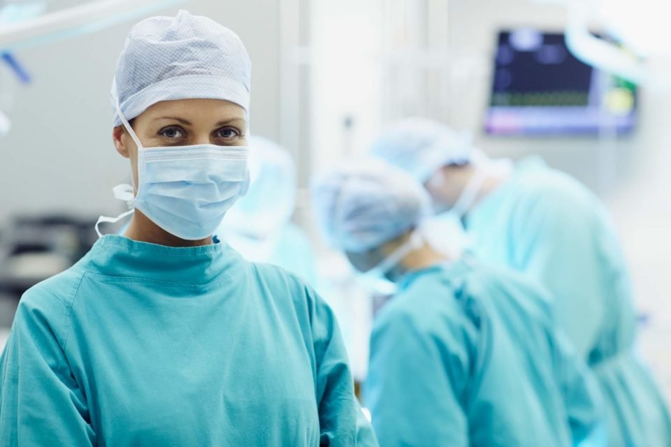 Foto mostra mulher médica em centro cirúrgico com equipe médica atrás dela - Metrópoles