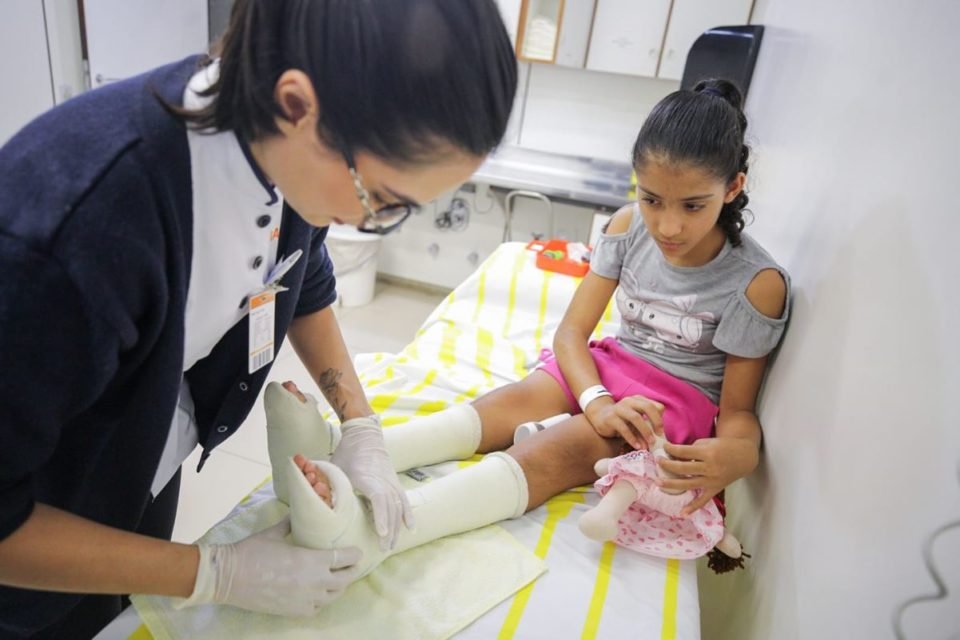 Foto de menina com pernas engessadas e brinquedos em hospital - Metrópoles