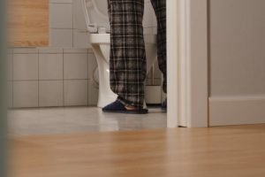 Foto colorida de pessoa usadno calça xadrez e pantufa enquanto está de pé na frente de vaso sanitário - Metrópoles