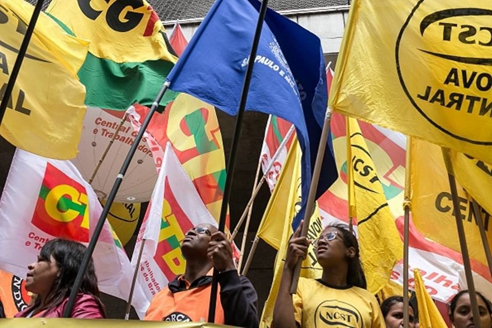 Imagem de manifestação de centrais sindicais, com militantes segurando bandeiras amarelas, vermelhas, verdes e azuis - Metrópoles