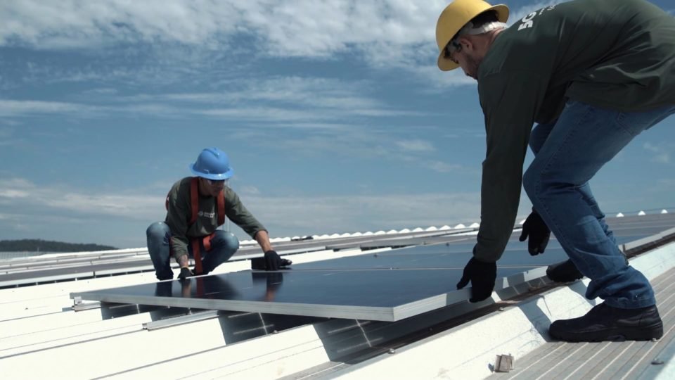 Fotografia colorida de dois homens instalando um painel de energia solar