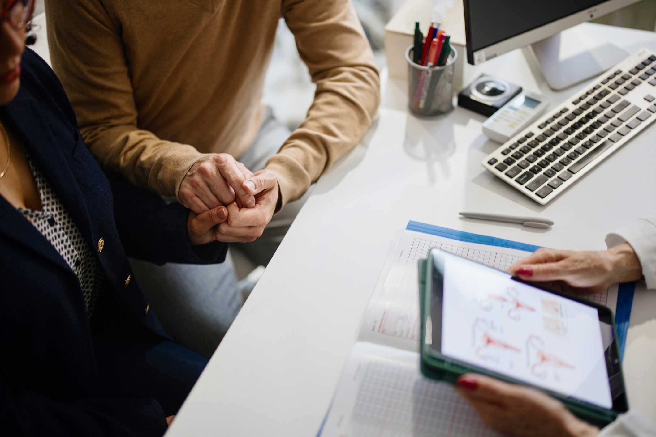 Foto mostra casal em consulta médica de mãos dadas