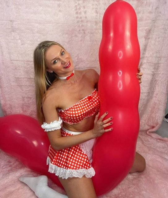 Foto colorida de uma mulher montada em um bal&atilde;o gigante vermelho e com formato f&aacute;lico - Metr&oacute;poles