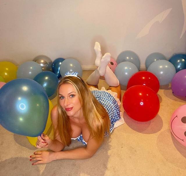 Foto colorida de uma mulher deitada no ch&atilde;o com um bal&atilde;o na m&atilde;o e v&aacute;rios outros bal&otilde;es coloridos espalhados no ch&atilde;o - Metr&oacute;poles