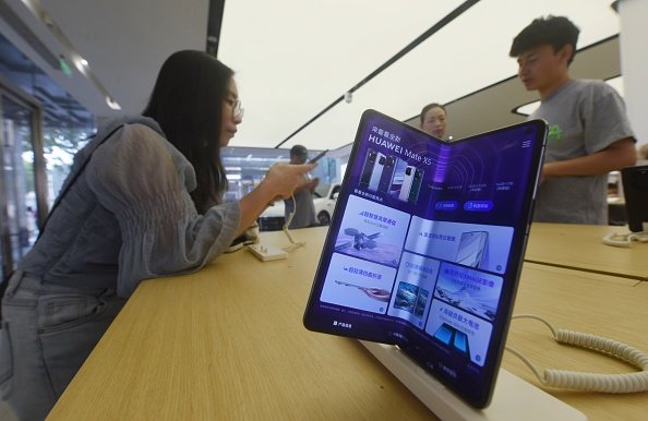 Consumidores chineses em loja da Huawei, mexendo em telefones celulares sobre uma mesa. Em destaque, a imagem do telefone dobrável 5G - Metrópoles