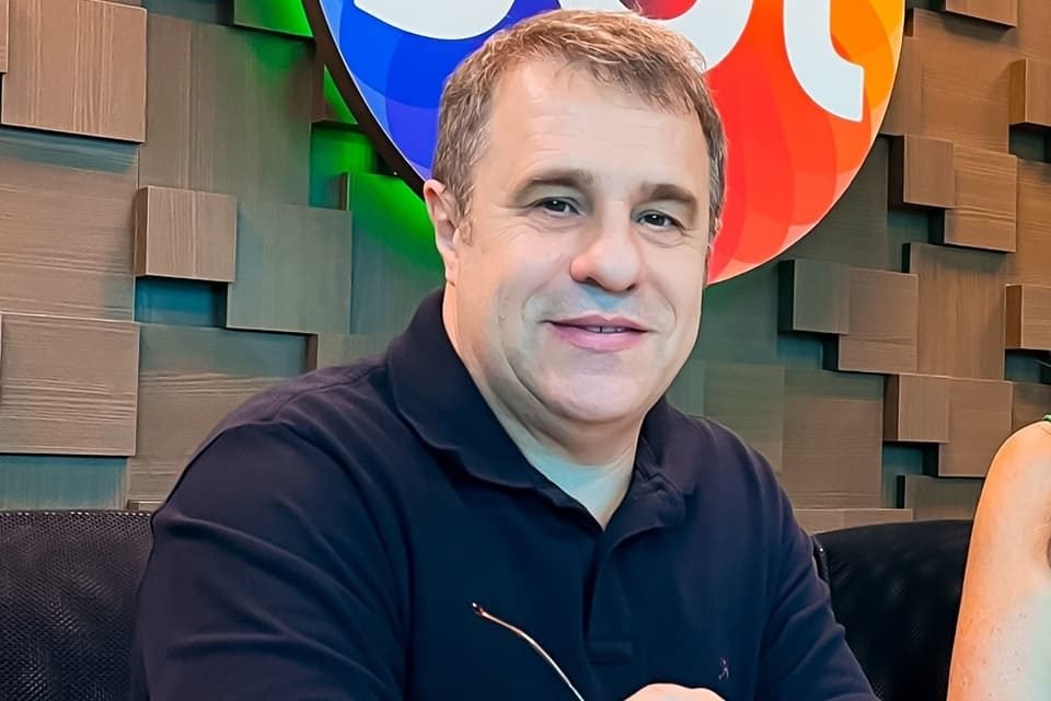 Fernando Pelegio posa de blusa preta perto da logo do SBT - Metrópoles