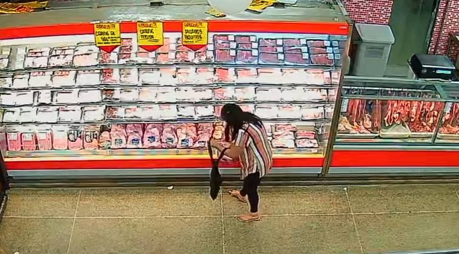 Imagem colorida de uma mulher com uma peça de carne em frente a um açougue de mercado - Metrópoles