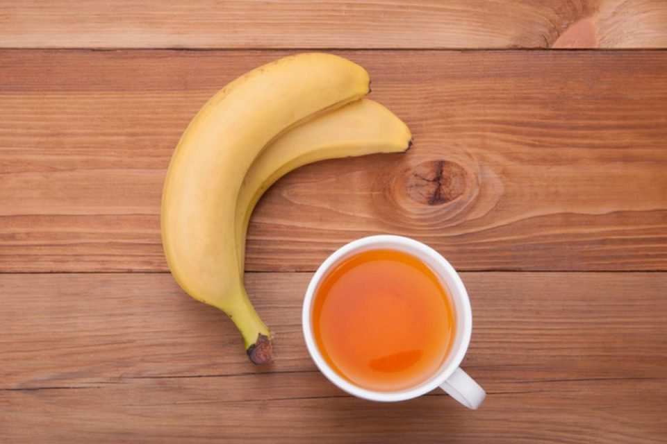 Foto colorida de mesa de madeira com banana e chá de banana em cima - Metrópoles