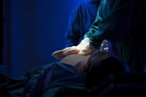 Imagem mostra close das mãos de uma pessoa de luvas fazendo massagem cardíaca em paciente deitado - Metrópoles