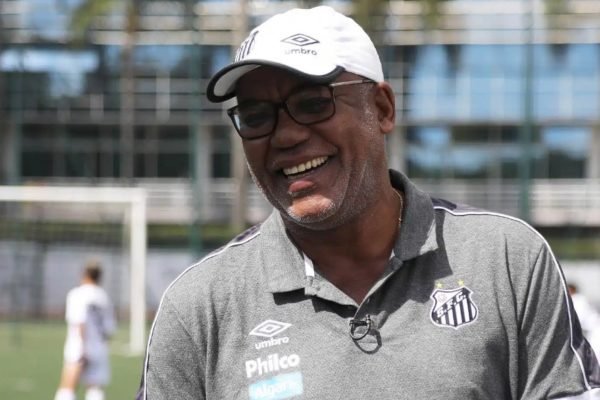 foto colorida mostra Serginho Chulapa usando boné branco do Santos, camiseta escura do clube, óculos e sorrindo - Metrópoles