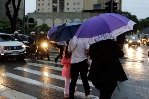 foto colorida de pedestres atravessando rua em São Paulo com guarda-chuvas - Metrópoles