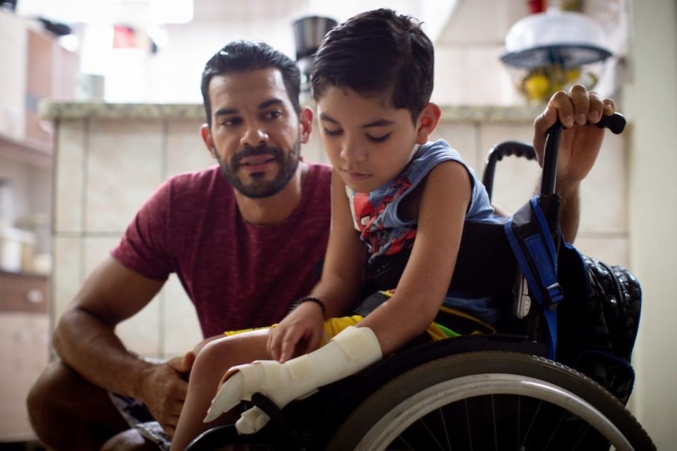 Imagem colorida de homem junto com o seu filho, que ficou tetraplégico após atropelamento