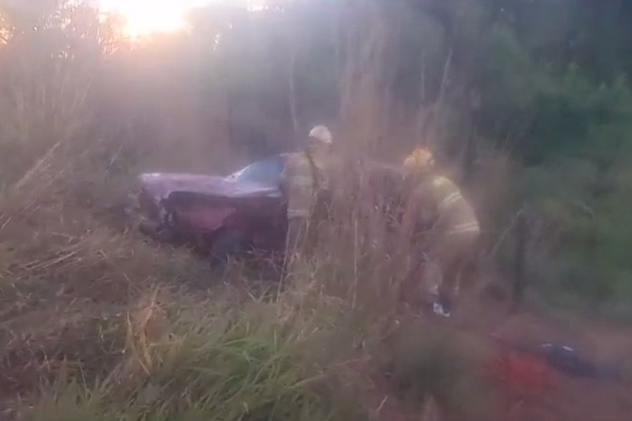 Bombeiros trabalham em área de matagal em carro destruído