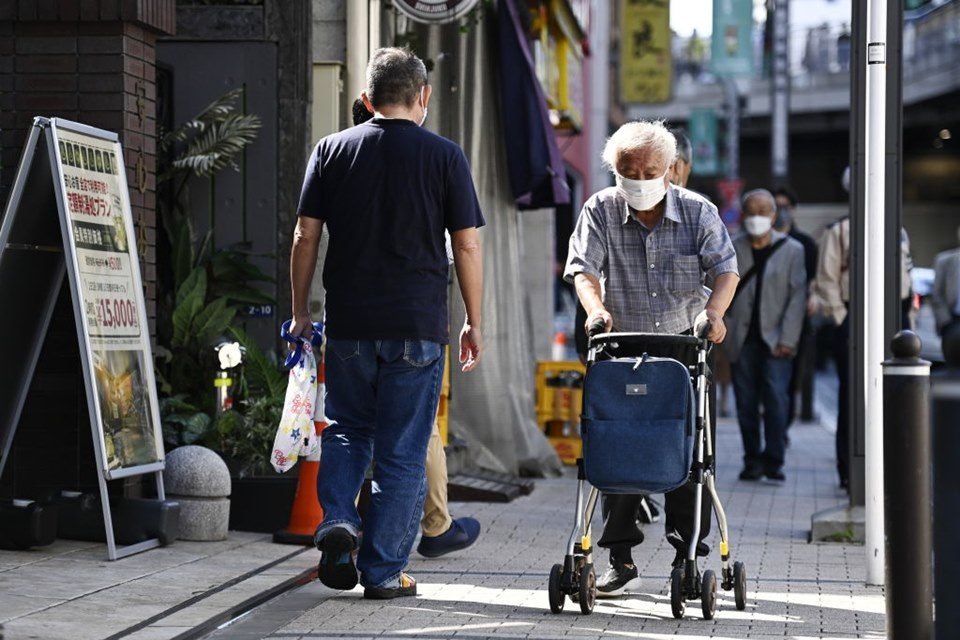 Imagem colorida de idoso caminhando em calçada do Japão com auxílio de um andador - Metrópoles