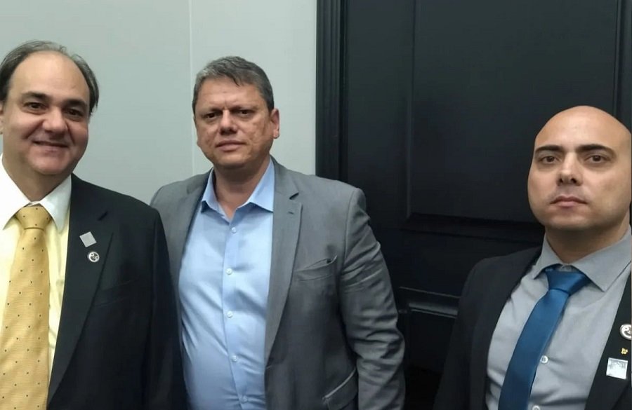 Fotografia colorida de Tarcísio de Freitas entre dois diretores - Metrópoles