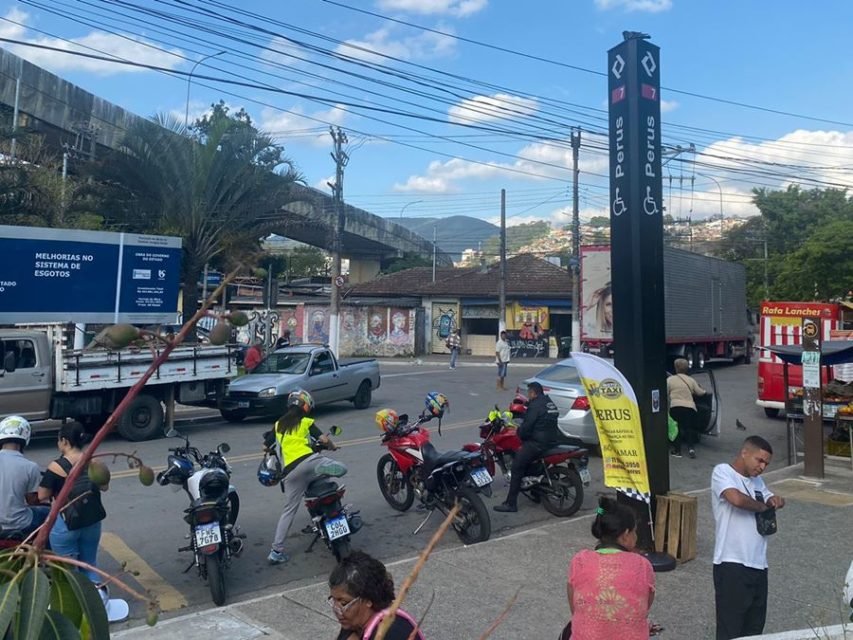Imagem colorida mostra calçada na frente da estação Perus da rede de trens, com mototáxis estacionados na frente