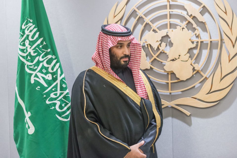 Imagem colorida do príncipe Mohammed bin Salman em pé em frente a bandeira da Arábia Saudita e do emblema da ONU - Metrópoles