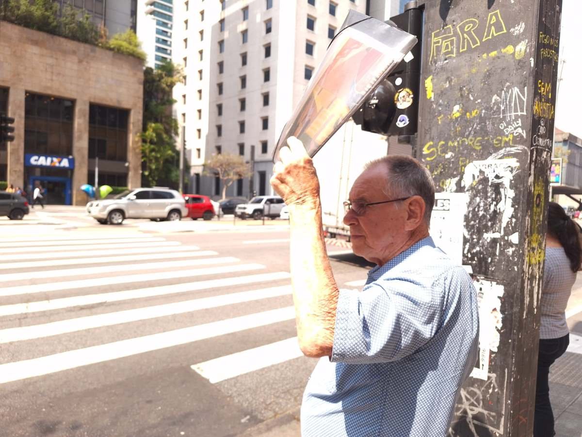 foto colorida mostra idoso se protegendo do sol e do calor com jornal em trecho da Avenida Paulista - Metrópoles