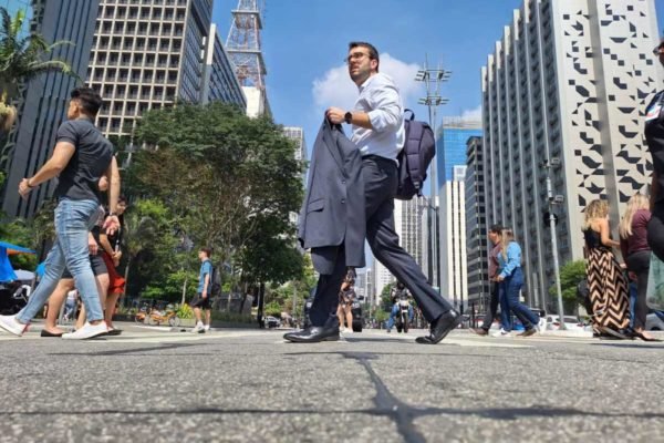foto colorida mostra homem caminhando sob sol com paletó na mão em trecho da Avenida Paulista - Metrópoles