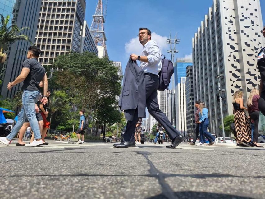 foto colorida mostra homem caminhando sob sol com paletó na mão em trecho da Avenida Paulista - Metrópoles