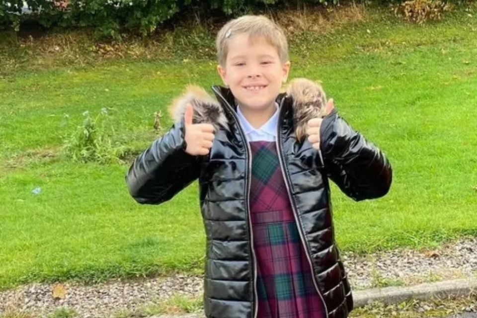 Foto colorida de um menino com casaco e vestido - Metrópoles