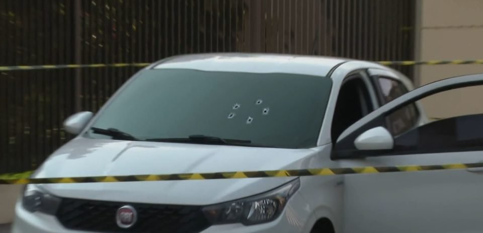 Imagem colorida de carro branco com para-brisa com marcas de bala - Metrópoles
