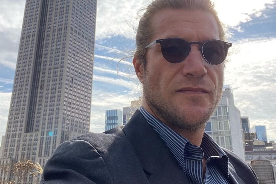 Ex-BBB Diego Alemão posa com um prédio ao fundo e usando blazer e óculos escuros - Metrópoles
