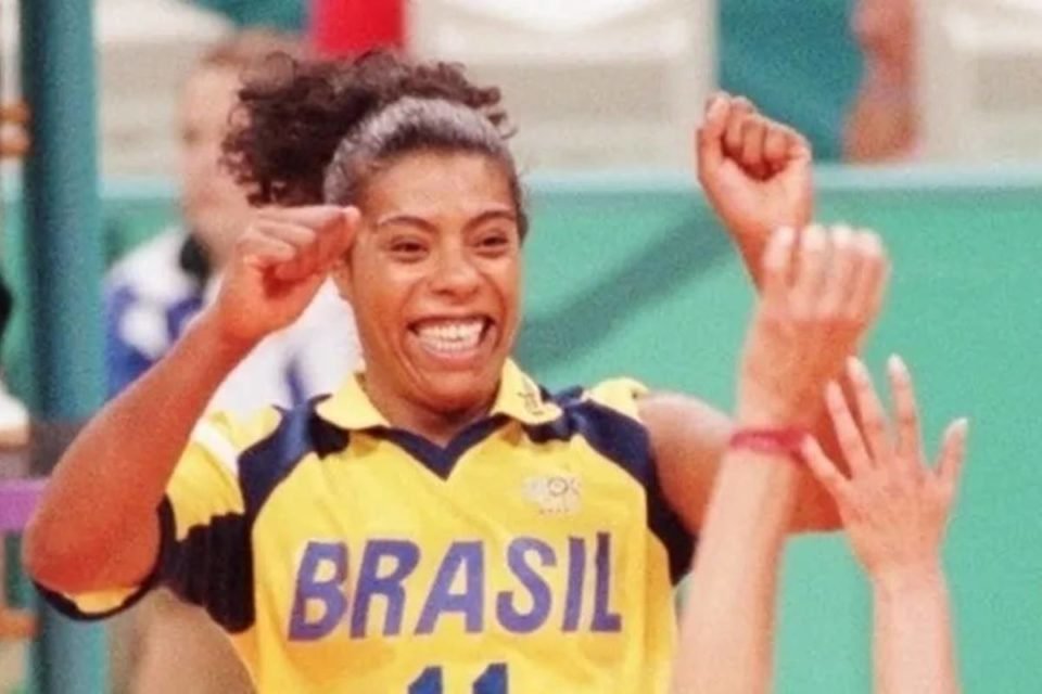 foto colorida de mulher negra com blusa do brasil sorrindo e comemorando em quadra de vôlei - metrópoles