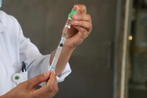 Imagem colorida de mãos segurando uma seringa e um recipiente com imunizante - Metrópoles