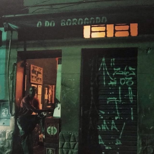 Imagem mostra homem em pé na frente do bar, à noite